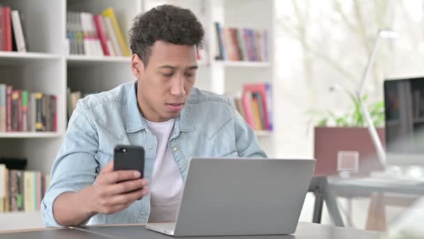 Молодой афроамериканец работает над смартфоном и ноутбуком — стоковое видео