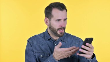 Portrait of Young Man getting Shock on Smartphone, Yellow Background