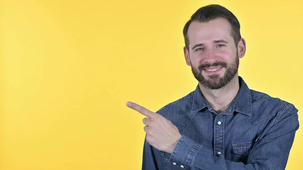 Portret van een jonge man wijzend naar product, gele achtergrond — Stockfoto