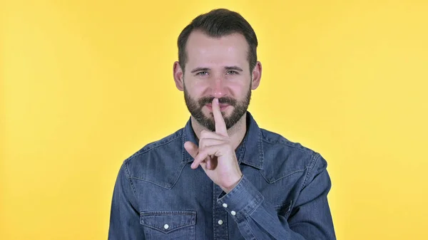 Porträtt av ung man sätta Finger på läppar, gul bakgrund — Stockfoto