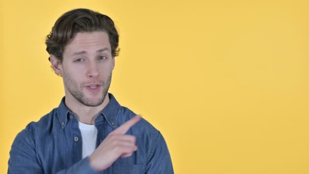 Fiatal férfi rámutatva a termék és beszél a sárga háttér — Stock videók