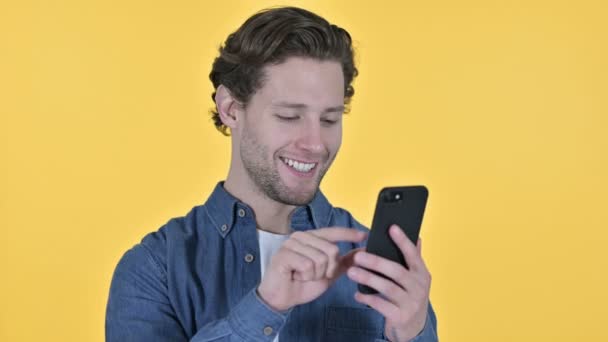 Portré fiatal férfi segítségével Smartphone sárga háttér — Stock videók
