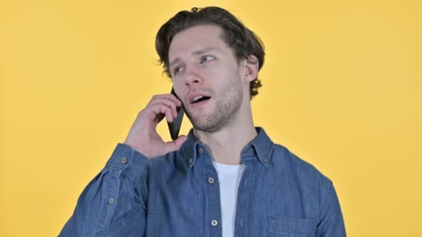 Портрет молодого человека, говорящего на смартфоне на жёлтом фоне — стоковое видео