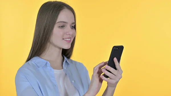 Vidám szép nő segítségével okostelefon, sárga háttér — Stock Fotó