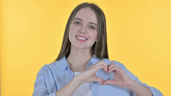 Forma de corazón con la mano por la mujer joven casual, fondo amarillo — Foto de Stock