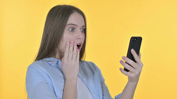 Mujer joven casual frente a la pérdida en el teléfono inteligente, fondo amarillo — Foto de Stock