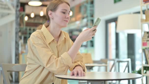 Junge Frau scrollt mit Smartphone in Café — Stockvideo