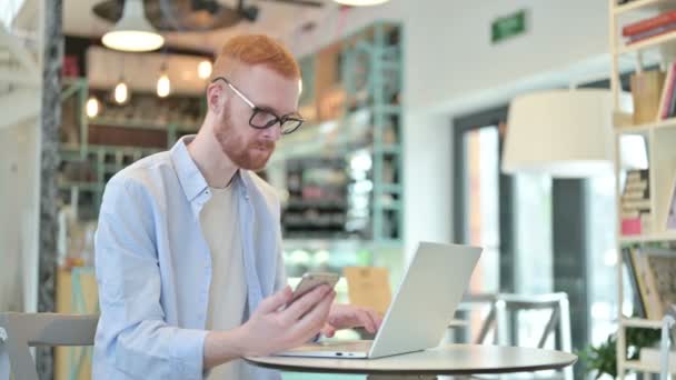 Rooie Man met behulp van Smartphone en Laptop in Cafe — Stockvideo