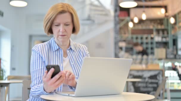 Smartphone användning av Creative Old Woman med laptop i Cafe — Stockvideo