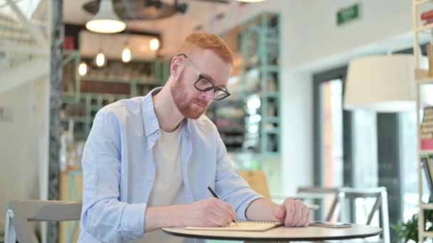Серьезный рыжеволосый занимается бумажной работой в кафе — стоковое видео