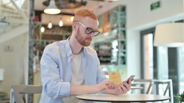 Εστιασμένη Redhead Man χρησιμοποιώντας Smartphone στο Cafe — Αρχείο Βίντεο