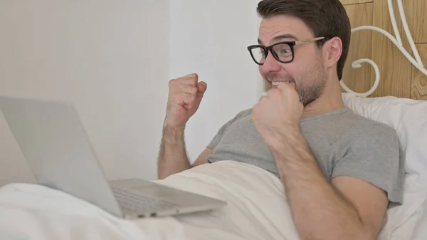 Jovem comemorando o sucesso no laptop na cama — Fotografia de Stock