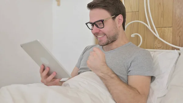 Joven celebrando el éxito en la tableta en la cama —  Fotos de Stock