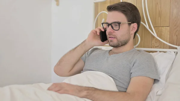 Unge man pratar på smartphone i sängen — Stockfoto