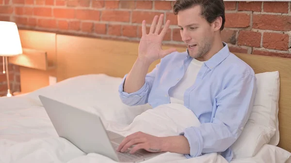 Junger Mann beim Videochat auf Laptop im Bett — Stockfoto