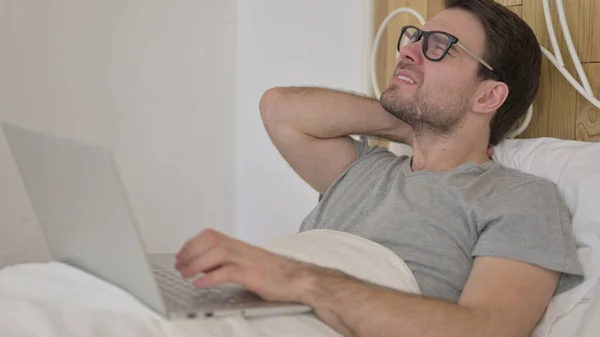 Νεαρός άνδρας που έχει πόνο στο λαιμό σε φορητό υπολογιστή στο κρεβάτι — Φωτογραφία Αρχείου
