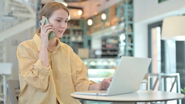 在咖啡店用智能手机与笔记本电脑交谈的年轻女性 — 图库照片