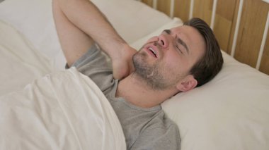 Yorgun genç adam yatakta boyun ağrısı çekiyor.
