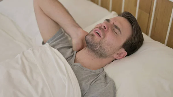 Zmęczony młody człowiek mając ból szyi w łóżku — Zdjęcie stockowe