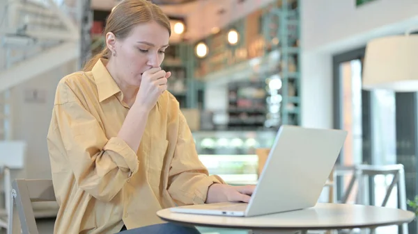 在咖啡店用笔记本电脑咳嗽的年轻女子 — 图库照片