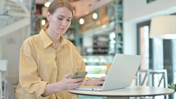 在咖啡店使用智能手机和笔记本电脑的年轻女性 — 图库照片