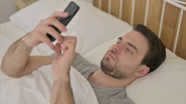 Hombre joven Desplazamiento en Smartphone en la cama —  Fotos de Stock