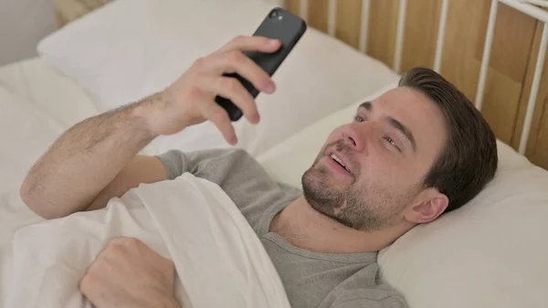 Unge man gör videochatt på smarttelefon i sängen — Stockfoto