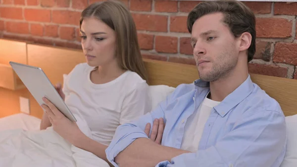 Angry Young Couple using Tablet in Bed — Stockfoto