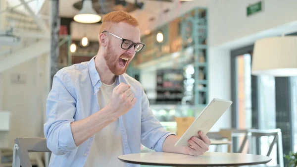 Redhead Man Celebrating Success on Tablet in Cafe