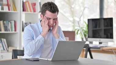 Baş ağrısı olan genç adam dizüstü bilgisayarda çalışıyor.