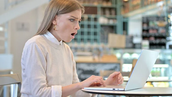Mladá žena reaguje na ztrátu na notebooku v kavárně — Stock fotografie