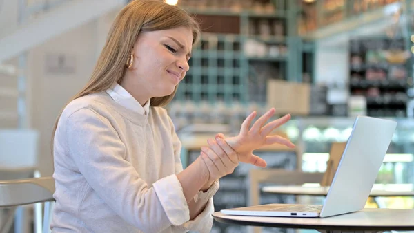 Giovane donna con dolore al polso utilizzando il computer portatile in Cafe — Foto Stock