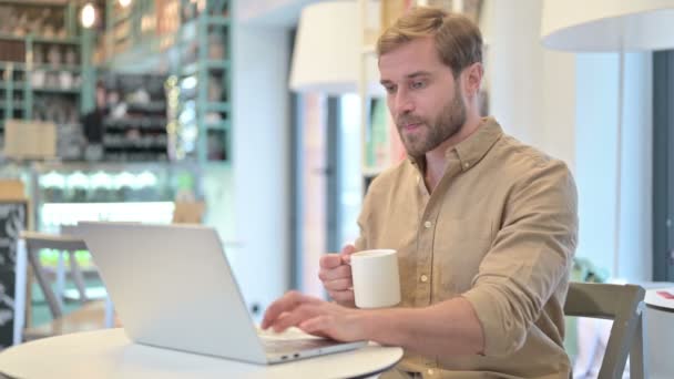 Привлекательный человек пьющий кофе работает на ноутбуке — стоковое видео