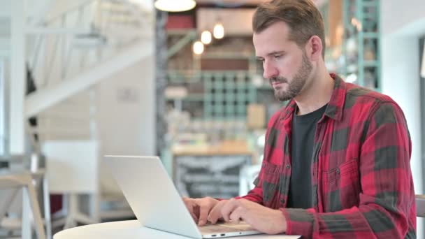 Schwerwiegender junger Mann mit Laptop blickt in Cafe auf Kamera — Stockvideo