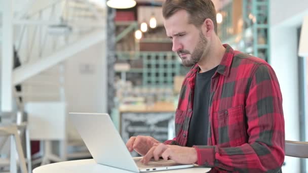 Młody człowiek z bólem głowy za pomocą laptopa w Cafe — Wideo stockowe