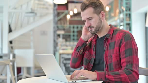 Unavený mladý muž s bolestí krku pomocí notebooku v kavárně — Stock video