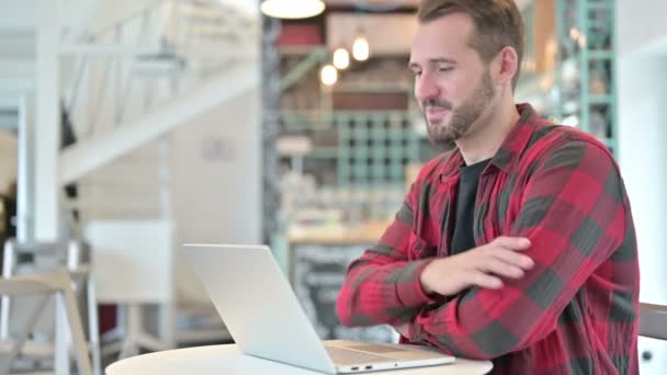 Chat vidéo sur ordinateur portable par attrayant jeune homme dans Cafe — Video