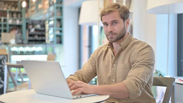 Jonge man op zoek naar camera tijdens het werken op laptop in Cafe — Stockfoto