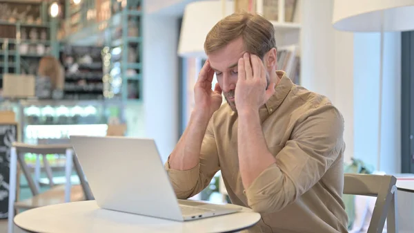 Młody człowiek z bólem głowy za pomocą laptopa w Cafe — Zdjęcie stockowe