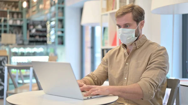 Jovem com máscara facial usando laptop no café — Fotografia de Stock