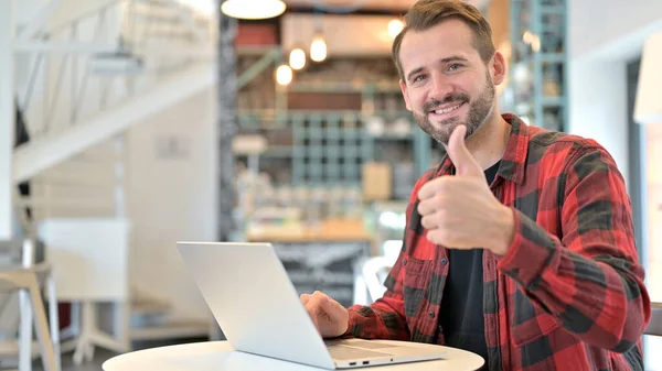 Tummen upp av positiv skägg ung man med bärbar dator i Café — Stockfoto