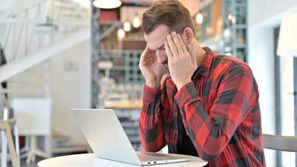 Junger Mann mit Bart und Kopfschmerzen benutzt Laptop im Café — Stockfoto