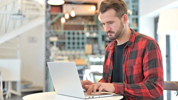 Broda młody człowiek pracuje na laptopie w Cafe — Zdjęcie stockowe