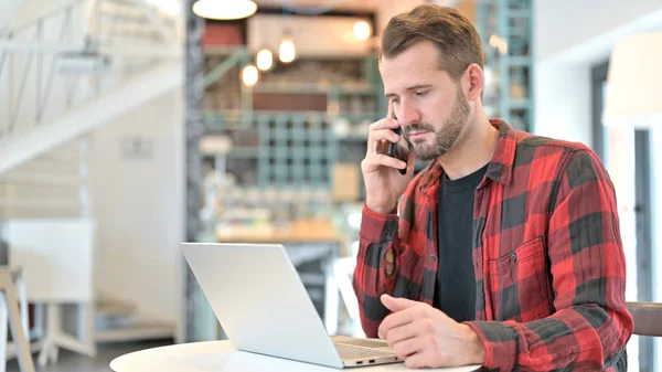 Baard jongeman met laptop praten op smartphone in Cafe — Stockfoto