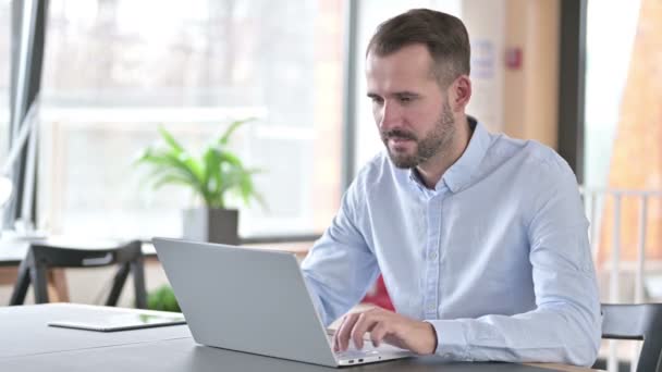 Młody człowiek świętuje sukces na laptopie w biurze — Wideo stockowe