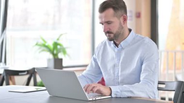 Dizüstü bilgisayarlı genç adam ofisinde Smartphone ile konuşuyor.