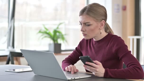 Jonge vrouw met laptop en smartphone op kantoor — Stockvideo