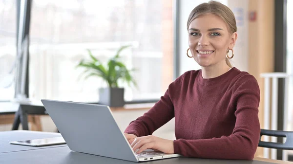 Junge Frau mit Laptop lächelt in Kamera im Büro — Stockfoto