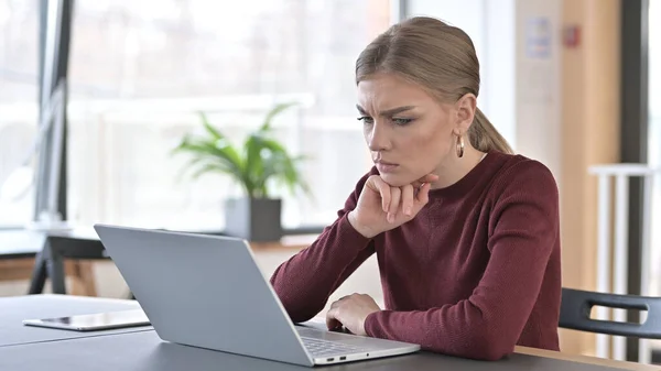 Pensive mladá žena čtení na notebooku v kanceláři — Stock fotografie