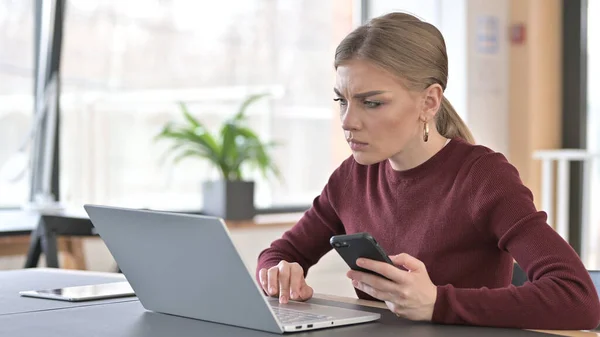 Jovem mulher usando laptop e smartphone no escritório — Fotografia de Stock